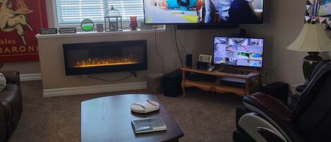 A living room with a fireplace, a large flat-screen TV mounted on the wall, a leather sofa, and a massage chair.