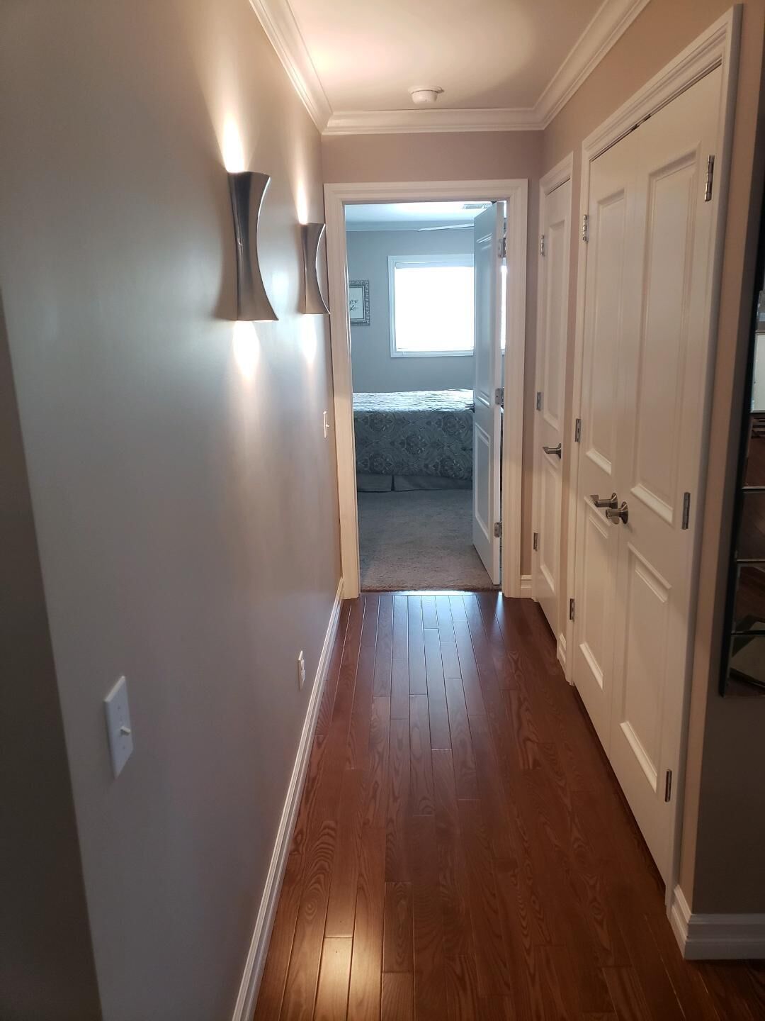 A hallway with wooden flooring, white walls, and a door leading to a bedroom.