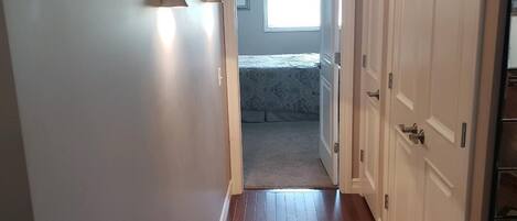 A hallway with wooden flooring, white walls, and a door leading to a bedroom.