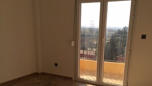 A room with a large sliding glass door leading to a balcony. The floor is tiled with a brown pattern. - Apartment in a private residence with caretaker (Souidania)