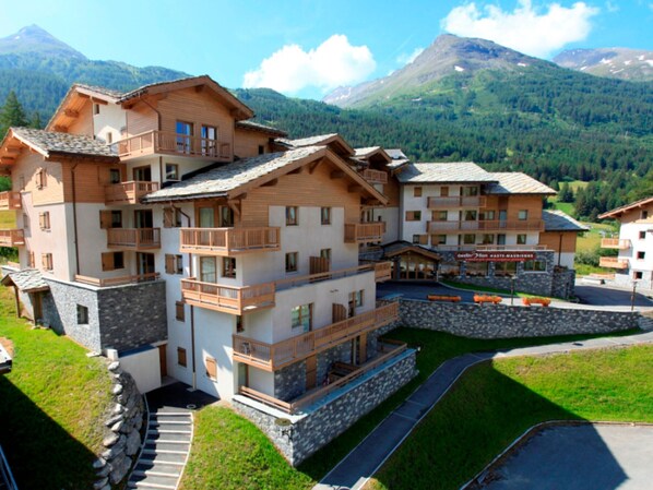Um hotel de vários andares com varandas, fachada de pedra e vista para as montanhas.