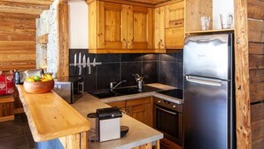 A kitchen with wooden cabinets, a central island, a refrigerator, and a stone wall.