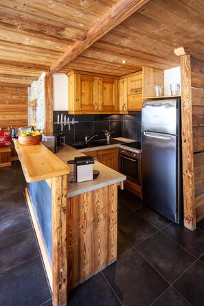 A kitchen with wooden cabinets, a central island, a refrigerator, and a stone wall.