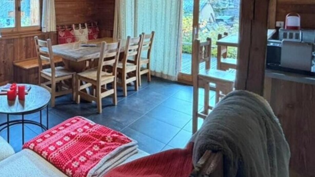 A wooden cabin interior with a dining area, a kitchen, and a view of the outdoors.