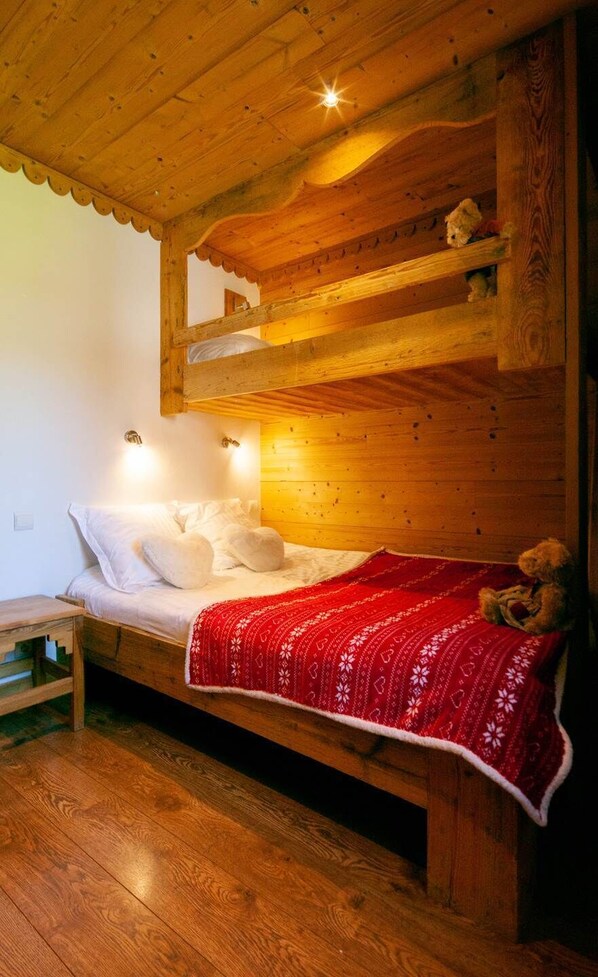 Un dormitorio de cabaña de madera con una cama litera, una manta roja y un osito de peluche.