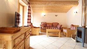 Un salon chaleureux avec un plafond en bois, un ensemble de canapés, un meuble en bois, une cheminée et un téléviseur.