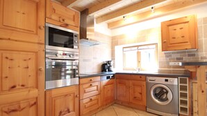 Une cuisine avec des meubles de rangement en bois, un four encastré, un lave-linge et une machine à café.