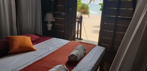A bed with a red and white striped bedspread, a rolled towel, and a single orange pillow. - Moon Isle Beach Bunglow (Nilaveli)