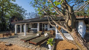A beachfront property with a covered patio, lounge chairs, and a large tree. - Moon Isle Beach Bunglow (Nilaveli)