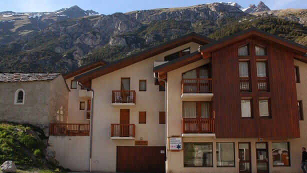 A two-story building with a wooden facade, balconies, and a mountain backdrop.