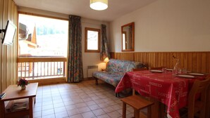 A cozy room with a sofa, a dining table set for two, a small table with a vase, and a window with curtains.