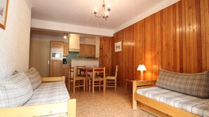 A cozy room with a wooden bed, a wooden sofa, a dining table with chairs, and a kitchen area. - Spacious apartment 5 ppl with balcony and wifi in Lanslebourg (Lanslebourg-Mont-Cenis)