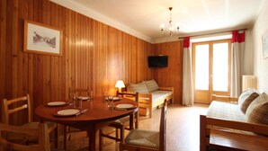 A wooden-paneled room with a dining table, chairs, a sofa, and a television. - Spacious apartment 5 ppl with balcony and wifi in Lanslebourg (Lanslebourg-Mont-Cenis)