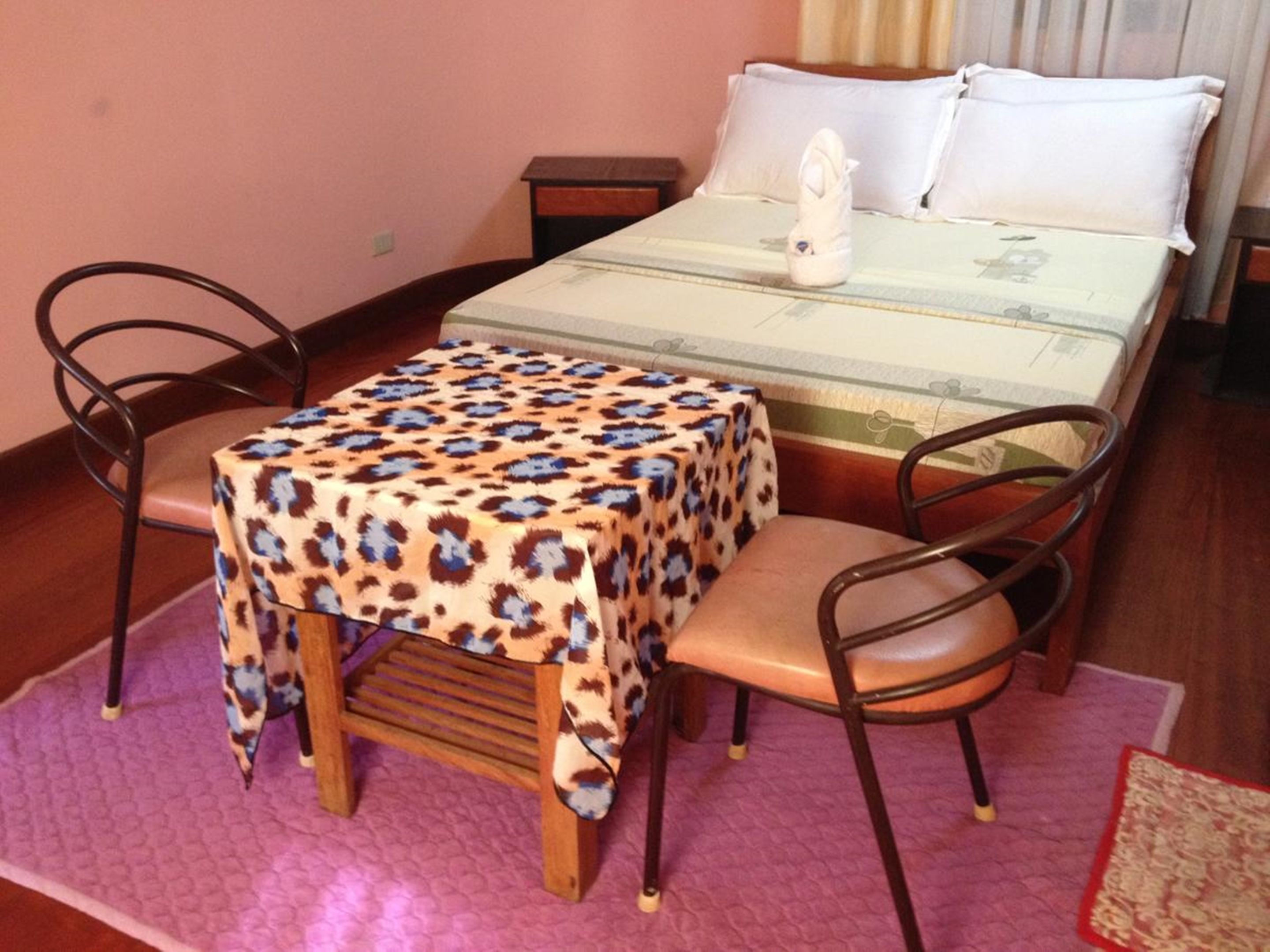 A room with a bed, a table with a leopard print tablecloth, two chairs, and a small nightstand.