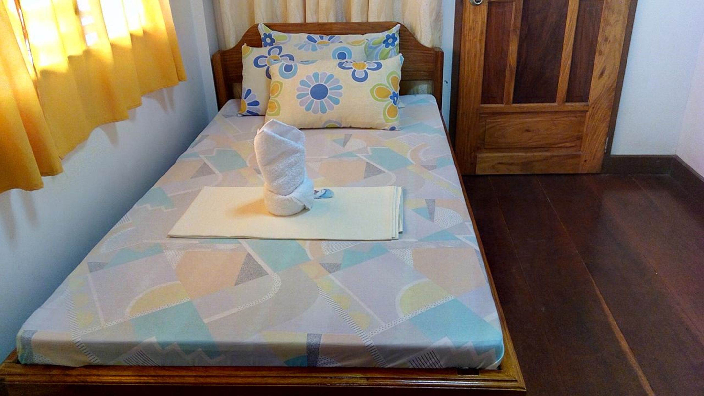 Una cama individual con una colcha estampada, un almohadón con diseño floral y una mesita de noche con un objeto blanco encima.