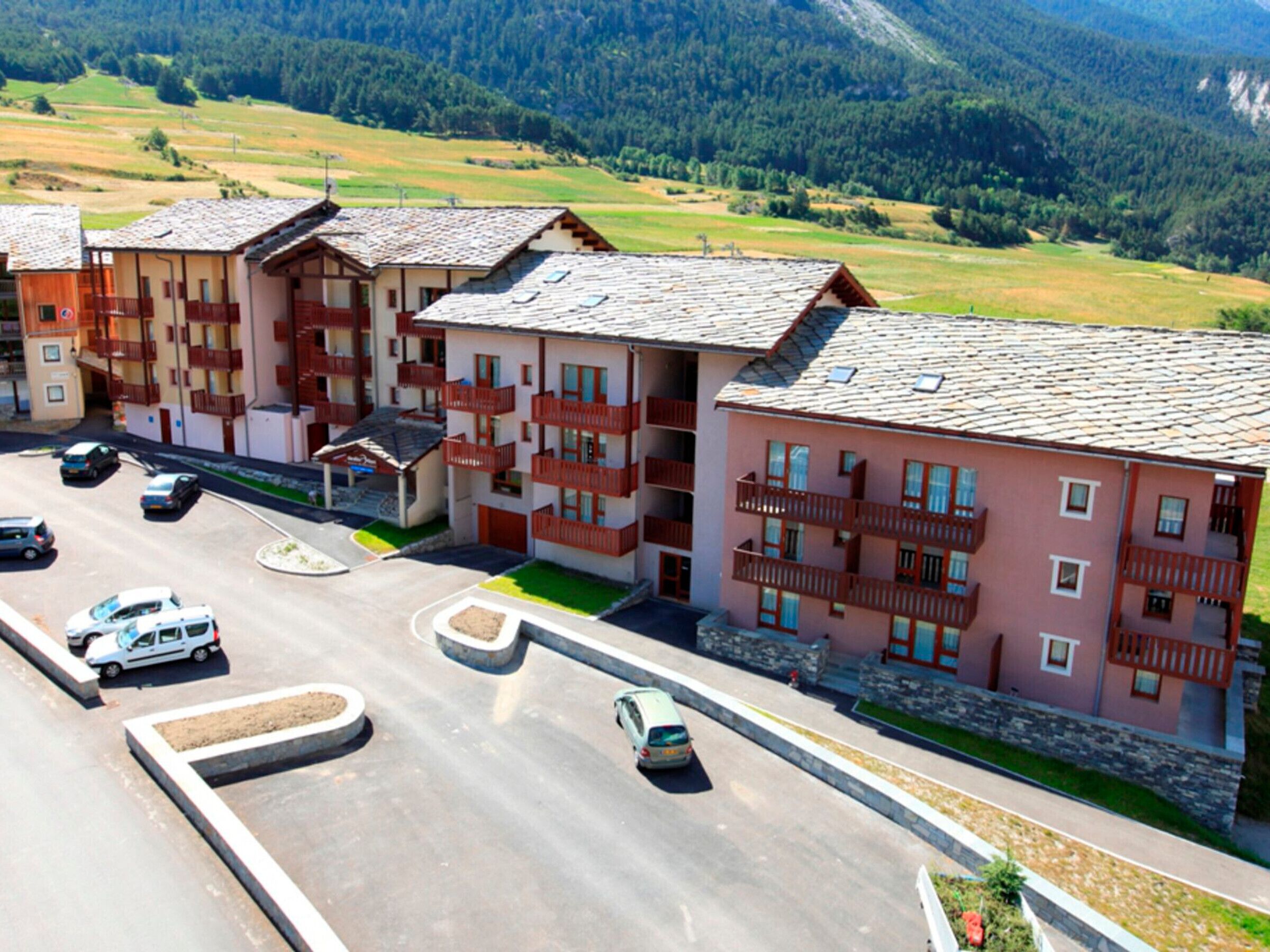 A multi-story hotel with balconies, a parking lot, and a mountainous backdrop.