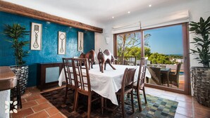 Un coin repas avec une table dressée pour quatre personnes, entourée de chaises, et une vue sur l’extérieur grâce à de grandes fenêtres.