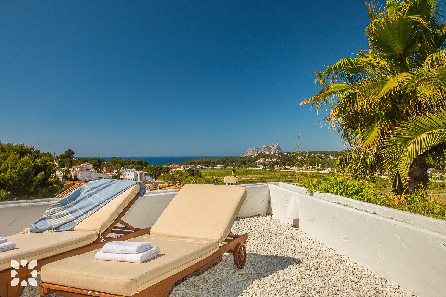 A rooftop terrace with lounge chairs and a view of the sea and distant landscape.
