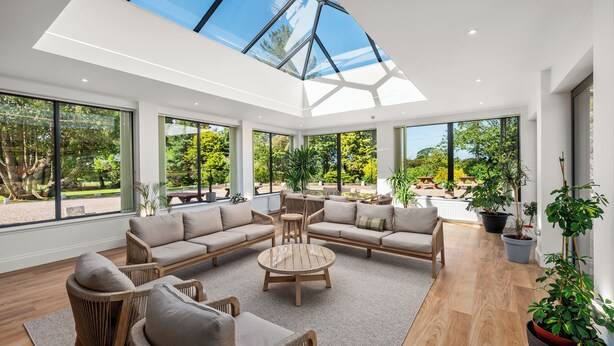 A spacious living area with a high ceiling and large windows, featuring a sectional sofa, a round coffee table, and several potted plants. - Victorian Mansion, fully refurbished, sleeps 24 guests in 12  ensuite bedrooms (Carnoustie)