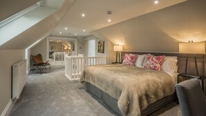 A bedroom with a large bed, a chair, a nightstand, and a lamp. There is a white railing and a door leading to another room. - Victorian Mansion, fully refurbished, sleeps 24 guests in 12  ensuite bedrooms (Carnoustie)