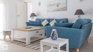 A modern living room with a teal sofa, a wooden coffee table, a small white side table, and a painting of a seascape on the wall. - Villa LADERA by Abahana Villas (Calp)