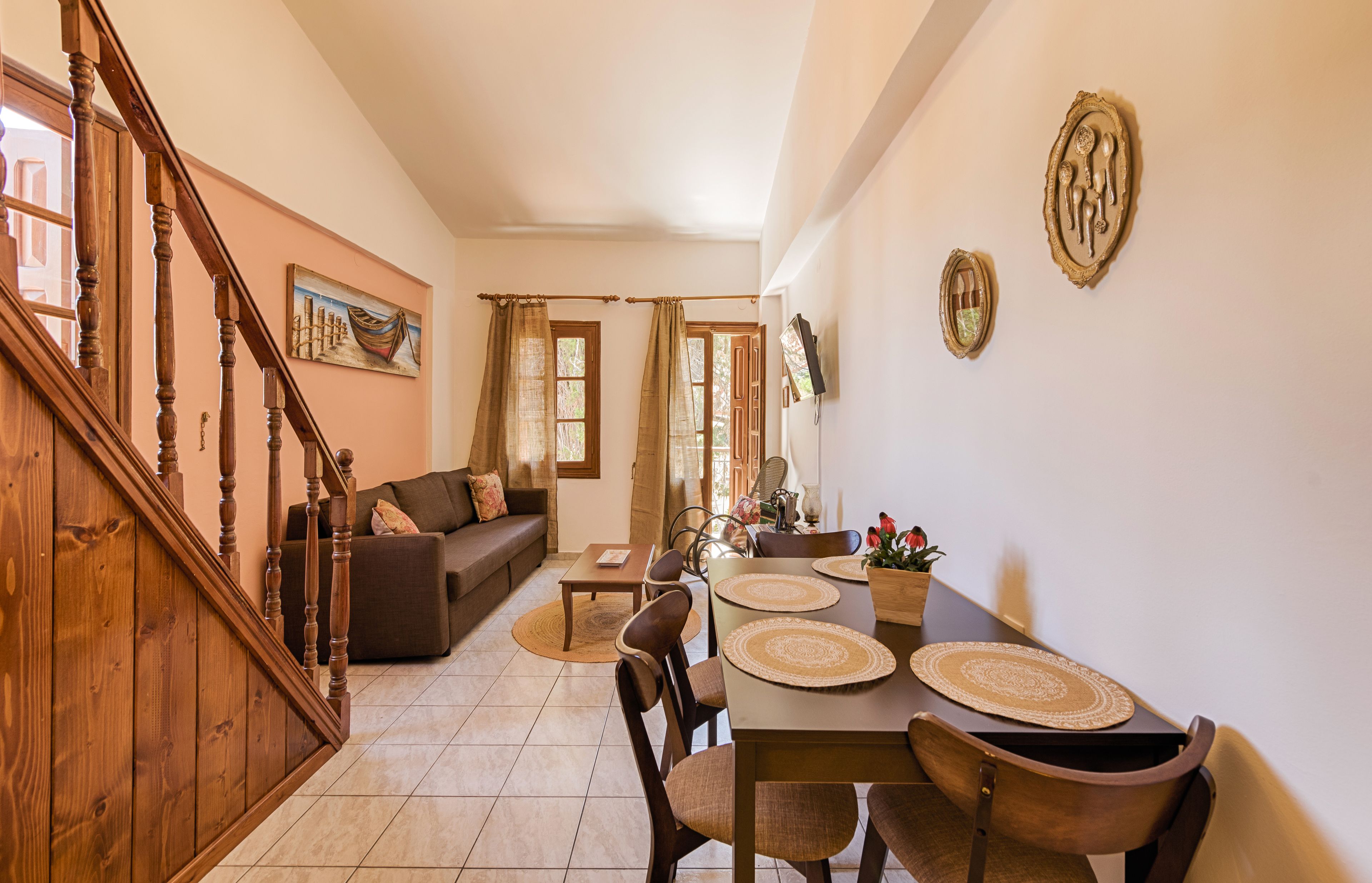 A spacious living area with a wooden staircase, a dining table with placemats, and a sofa with cushions.