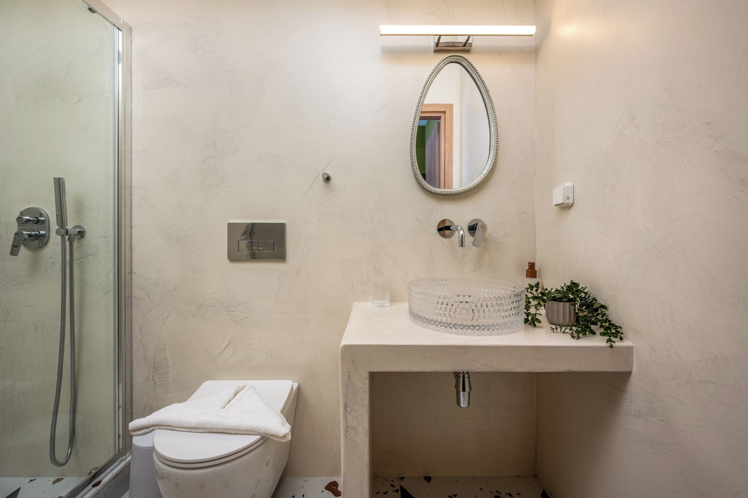 Un baño con cabina de ducha de vidrio, inodoro, lavabo con espejo y una pequeña planta en maceta.