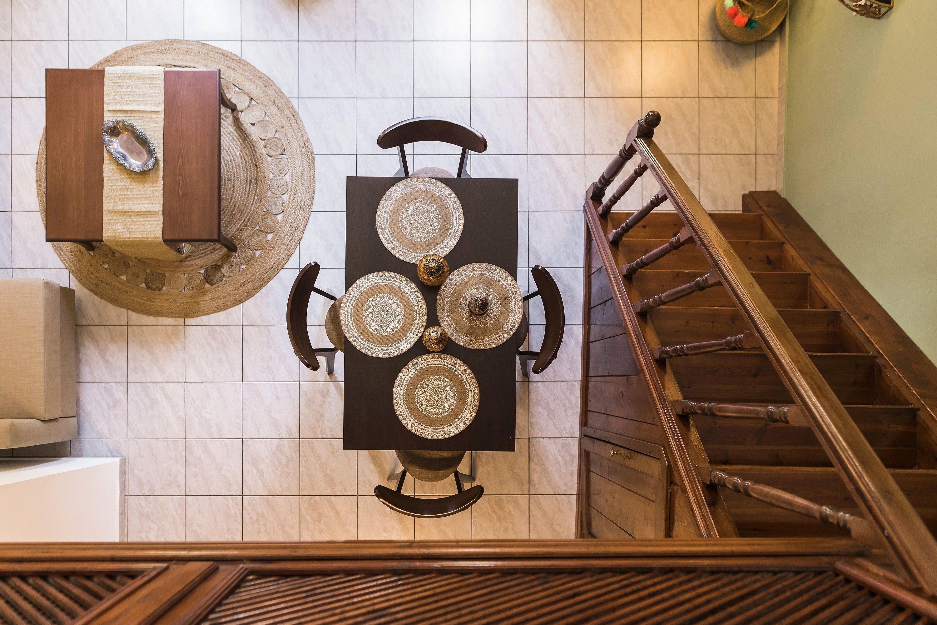 A dining area with a table set for four, a wooden staircase, and a wall-mounted decorative item.