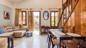 Amplia sala de estar con sofá, mesa de comedor y sillas. Una escalera con barandillas de madera conduce a un nivel superior.