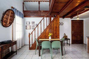 A dining area with a wooden staircase, a table with chairs, and a wall with framed pictures. - The Old Symi (Symi)