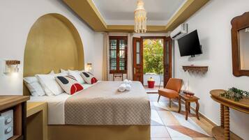 A hotel room with a bed, a TV, a chair, a small table, and a window with a view of greenery.