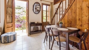 Un comedor con una mesa y sillas de madera, una mesita redonda con una planta y una escalera con barandillas de madera.