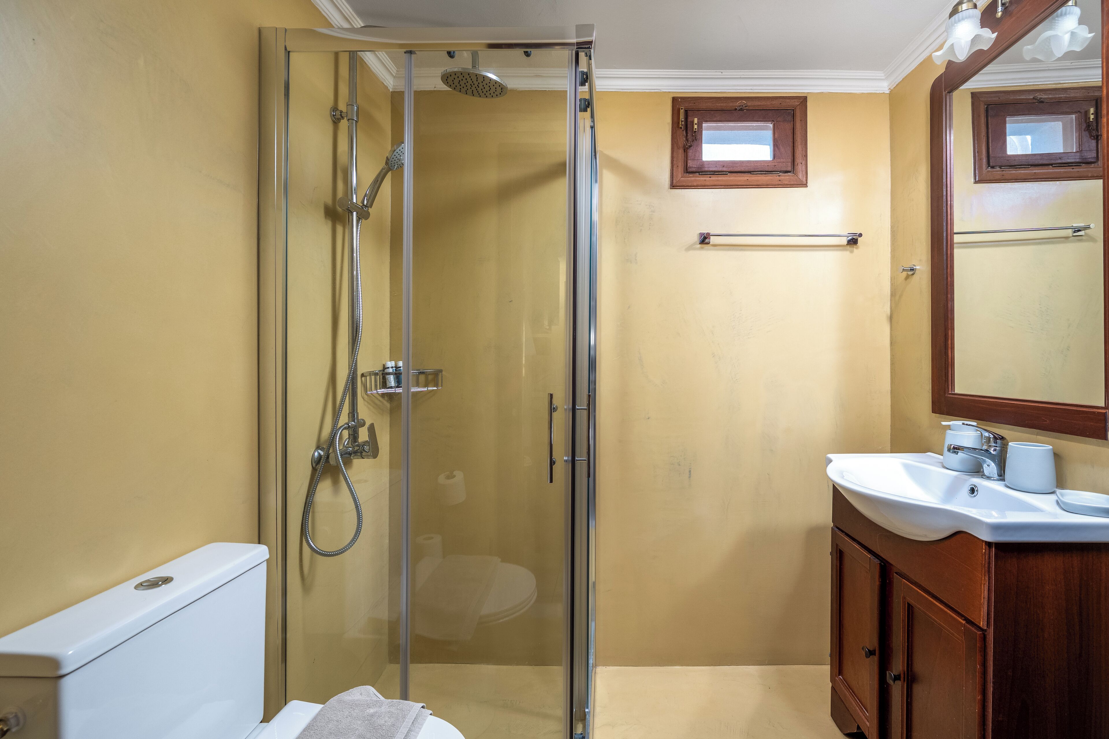 Un baño con cabina de ducha de vidrio, inodoro blanco y tocador de madera con espejo.