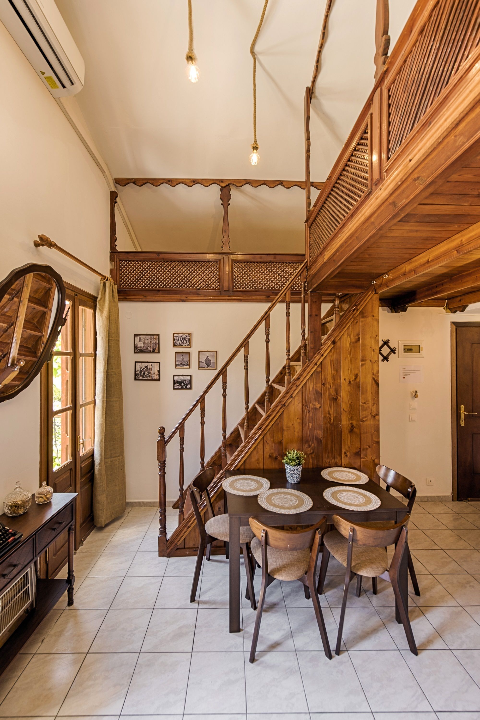 Uma sala de jantar com escada de madeira, mesa redonda com cadeiras e parede com quadros.