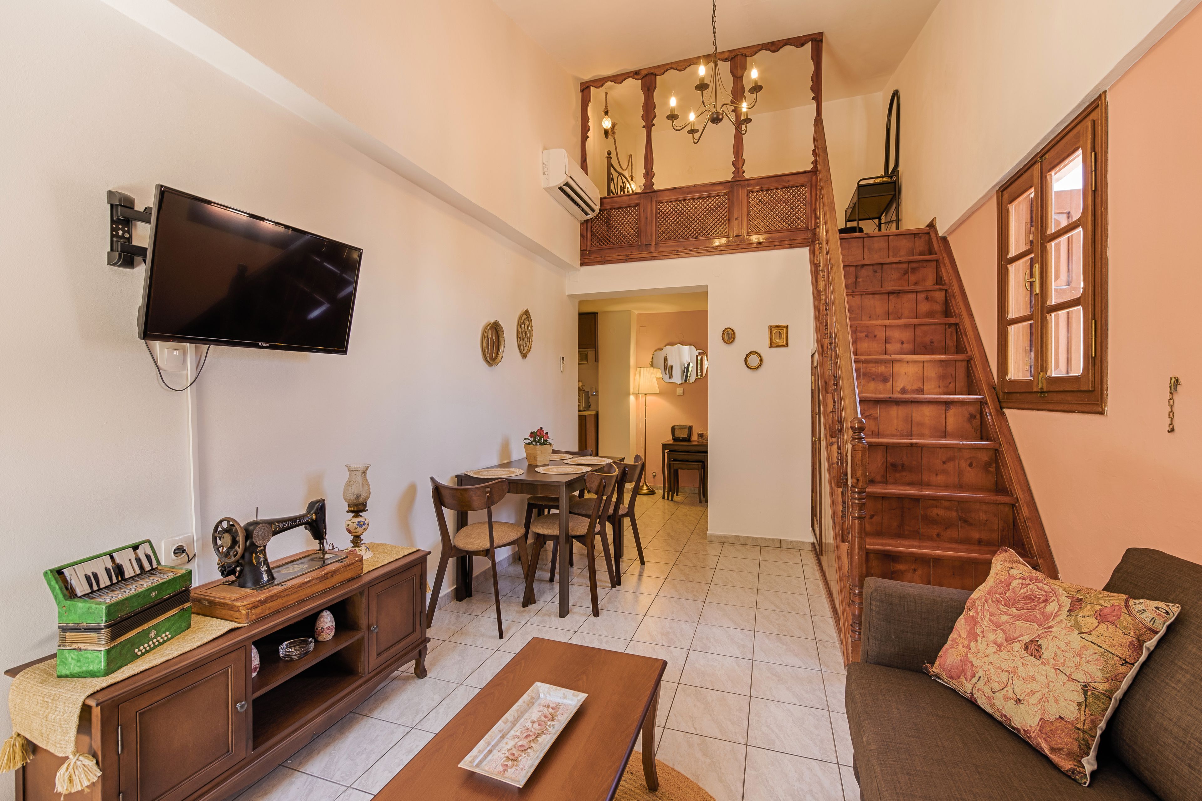 A living room with a flat-screen TV, wooden furniture, a dining area, and a staircase.