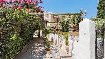 A narrow alley with a white wall on one side and a wooden fence on the other, leading to a building with a balcony.