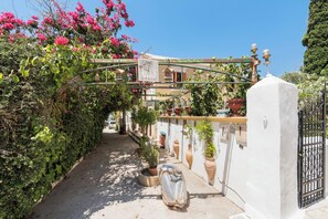 Une ruelle étroite, bordée d’un côté par un mur blanc et de l’autre par une clôture en bois, qui mène à un immeuble doté d’un balcon.