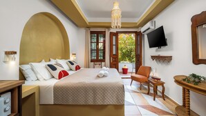 Habitación de hotel con cama, televisor, sillón, una mesita y ventana con vista a follaje.
