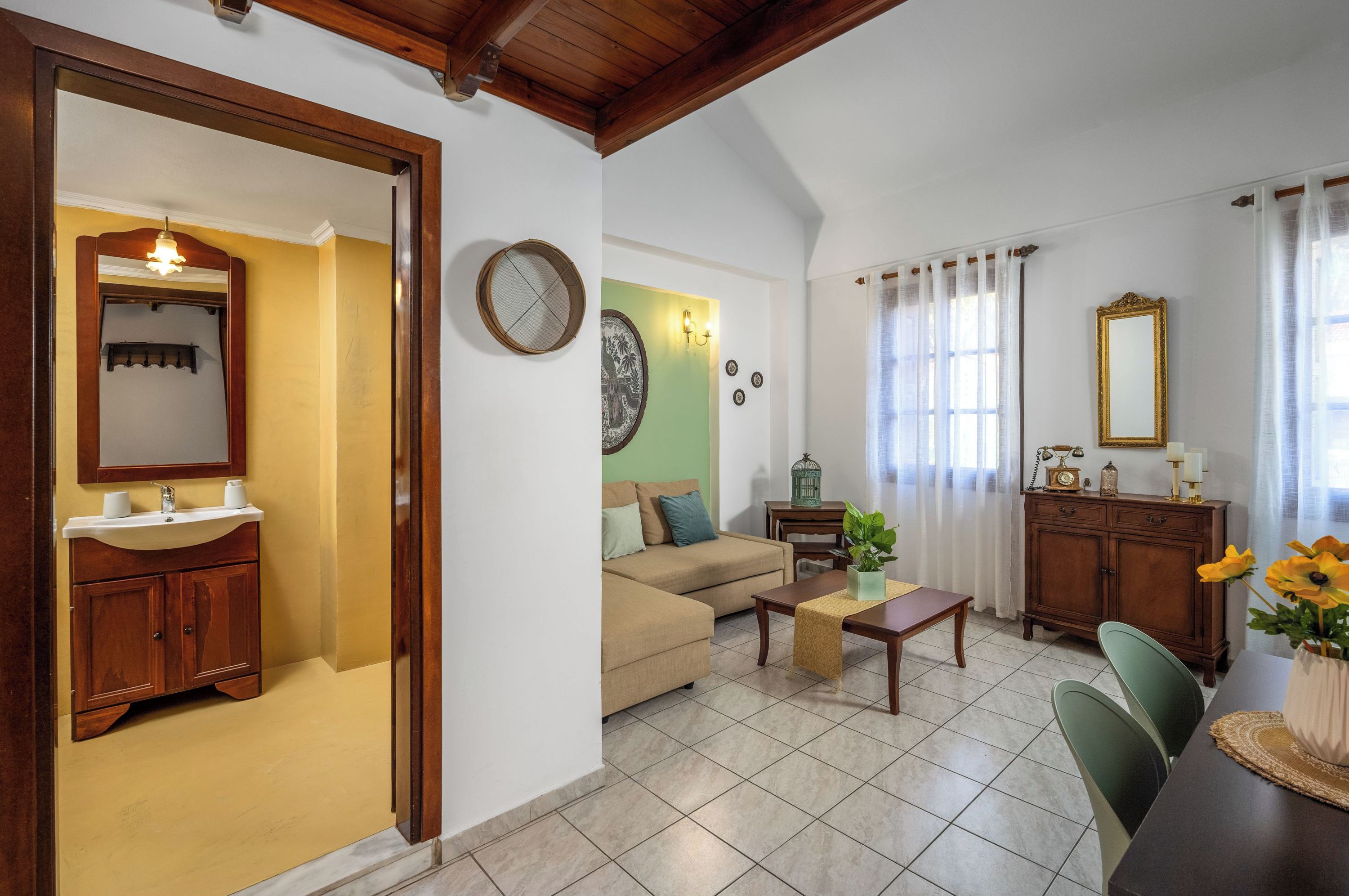 Sala de estar con sofá, mesa de centro y mesa de comedor. Hay un armario de madera con espejo y lavabo. En las paredes hay un reloj y objetos decorativos.