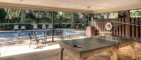 Un espace extérieur abrité comprenant une table de ping-pong, des chaises longues et une piscine.