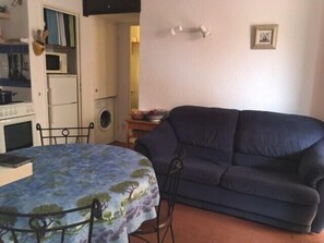 Un espace de vie compact comprenant une table à manger, un canapé, un lave-linge et un petit coin cuisine.