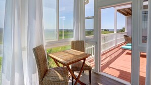 A covered patio with a table and chairs, a view of the ocean, and a wooden deck. - Heated Pool Access | 5*Clean | Flex Cancelation (Tybee Island)