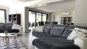 Een moderne woonkamer met een grote bank, een salontafel en een eethoek met stoelen.