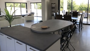 Een moderne keuken met een centraal eiland, een eetgedeelte met stoelen en grote ramen met uitzicht op de omgeving.