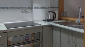 Cocina compacta con electrodomésticos de acero inoxidable, microondas, hervidor y lavabo.