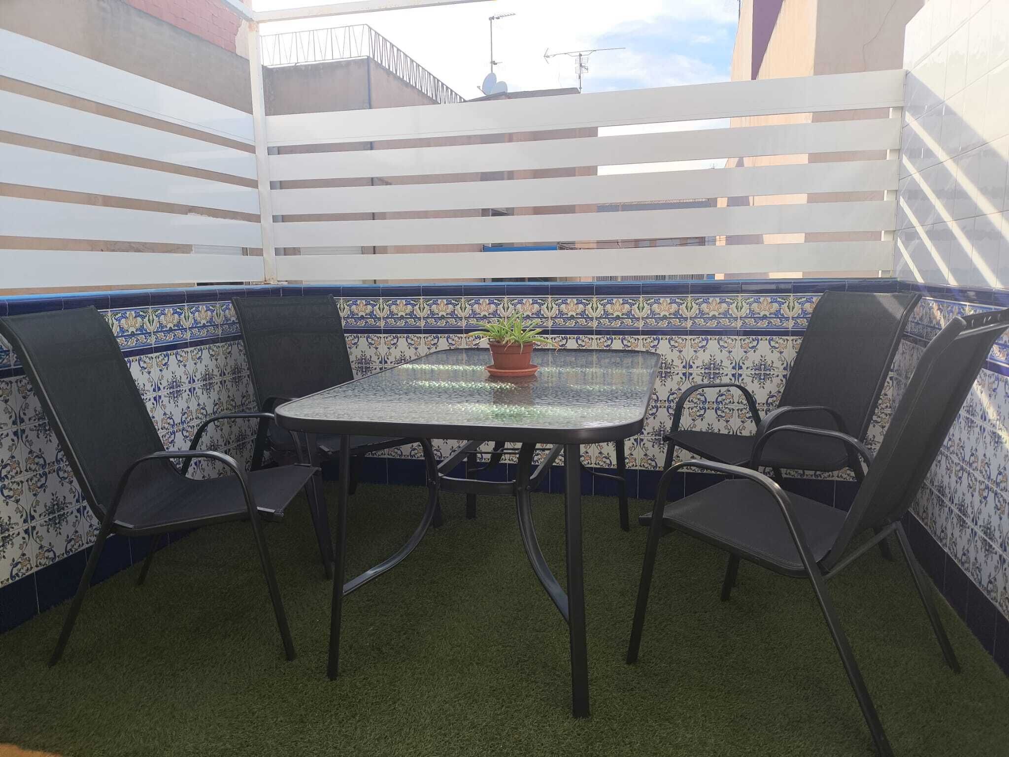 A small outdoor patio with a round table, four chairs, and a potted plant.