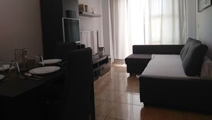 Una sala de estar con un sofá, una mesa de comedor dispuesta con platos, vasos y cubiertos, un televisor y un ventilador de techo.