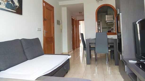 Una sala moderna con un sofá, un comedor con sillas, una cocina con refrigerador y un ventilador de techo.