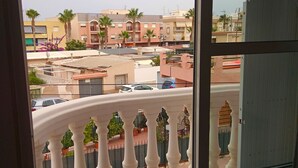 Un balcón con barandilla blanca curva, con vistas a una zona residencial con edificios y coches aparcados.