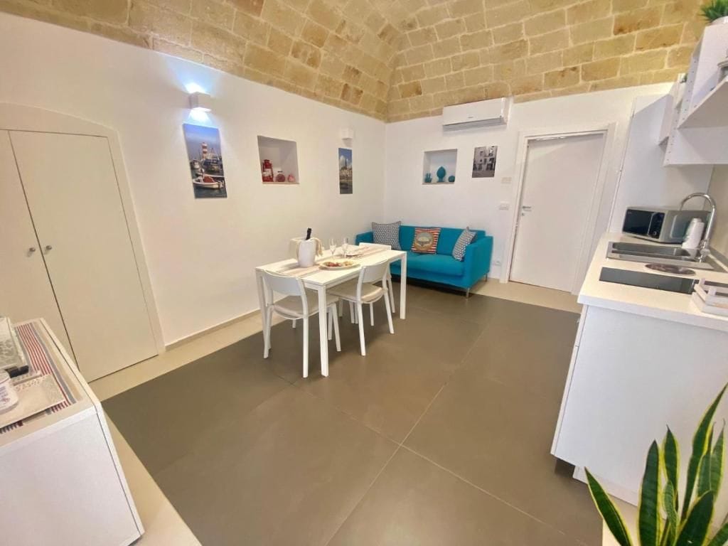 Un espacio habitable compacto con comedor, kitchenette y un sofá azul.